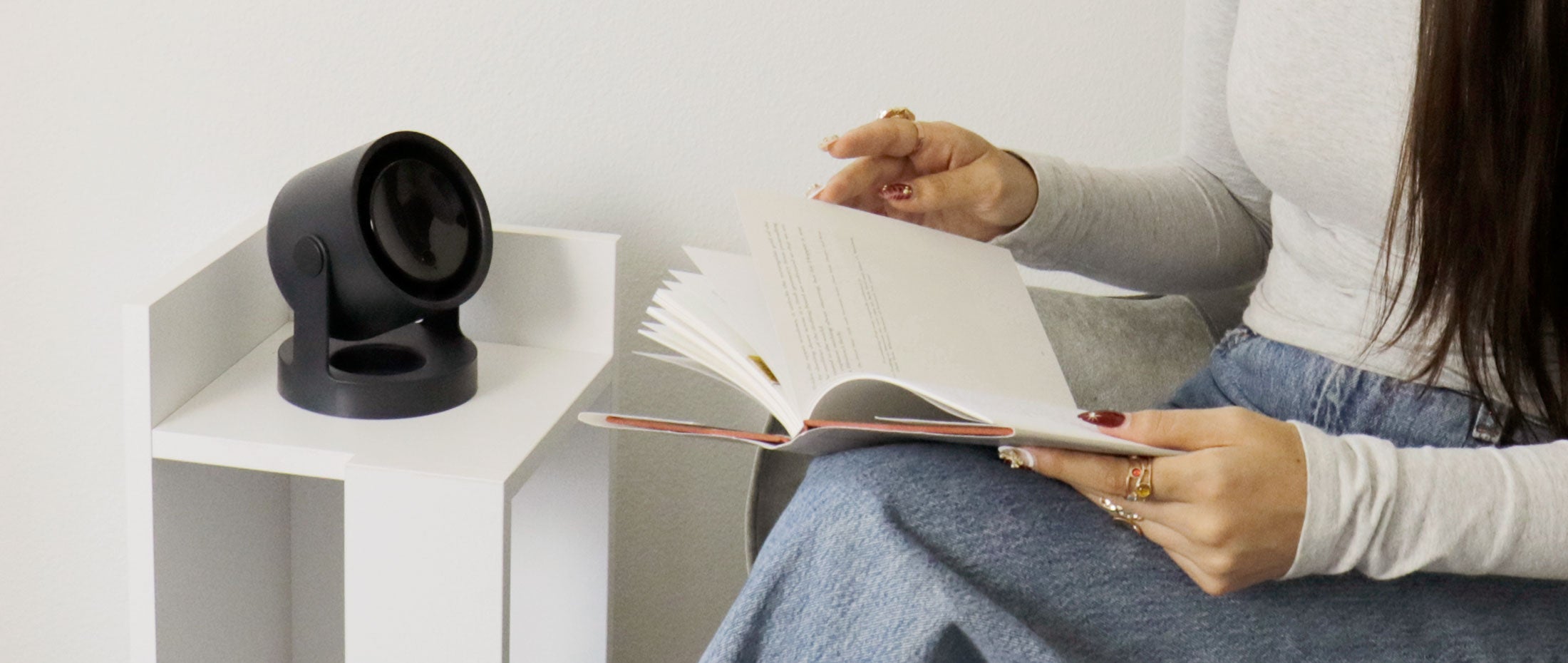 Person reading a book next to an Aluratek fan on a white shelf.